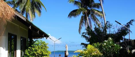 A tropical resort with a thatched-roof building, palm trees, a pathway leading to the beach, and a view of the ocean.