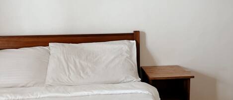 A bed with white linens, a wooden headboard, a wooden nightstand, and a beige towel arranged in a bow shape.