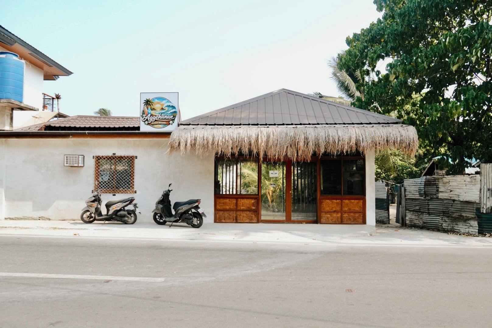 A building with a thatched roof, a signboard, and two parked scooters.