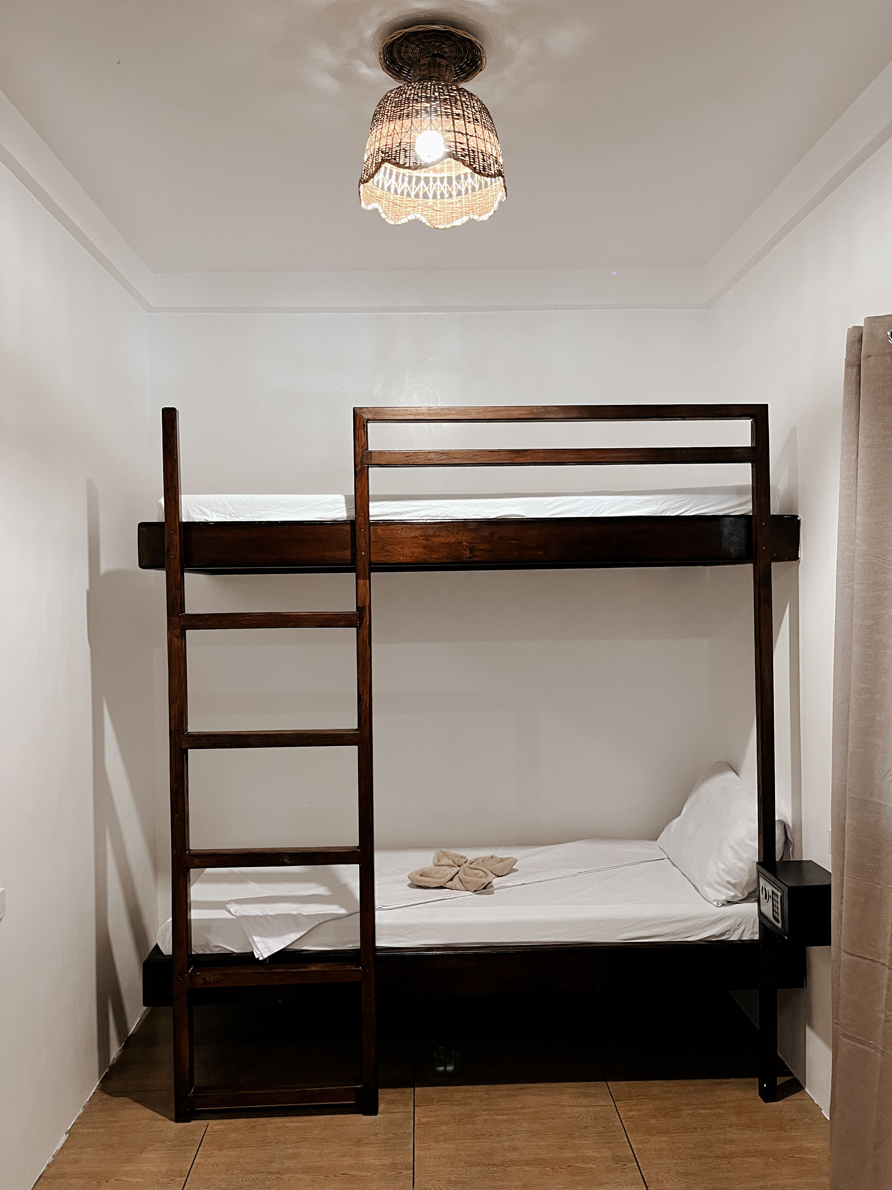 Una cama litera con escalera, una mesita de noche pequeña y una lámpara en el techo.