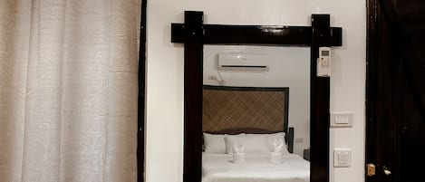 A hotel room with a bed, an air conditioning unit, a door, and a curtain.