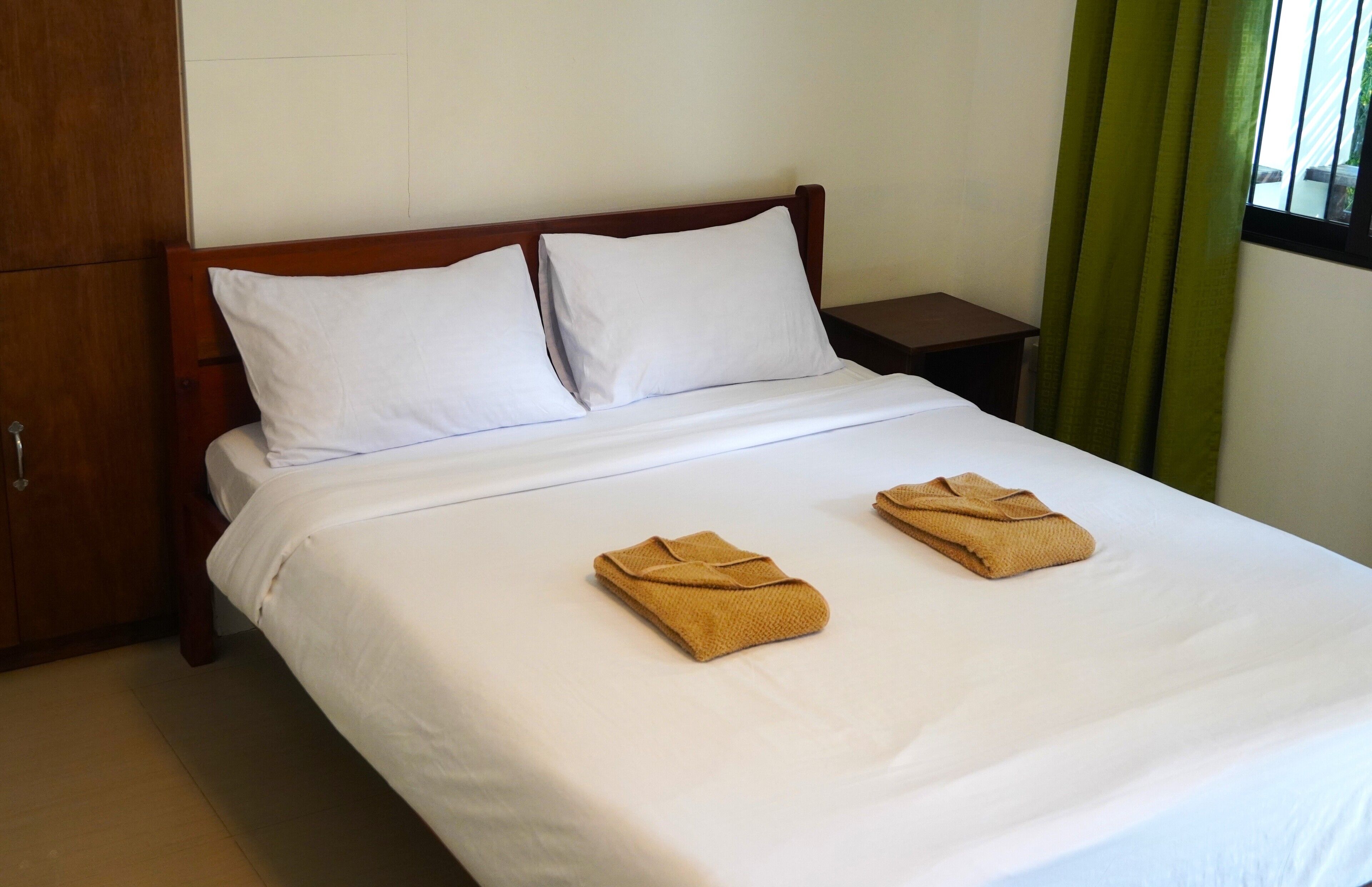 Habitación de hotel con cabecera de madera, ropa de cama blanca y dos toallas sobre la cama.