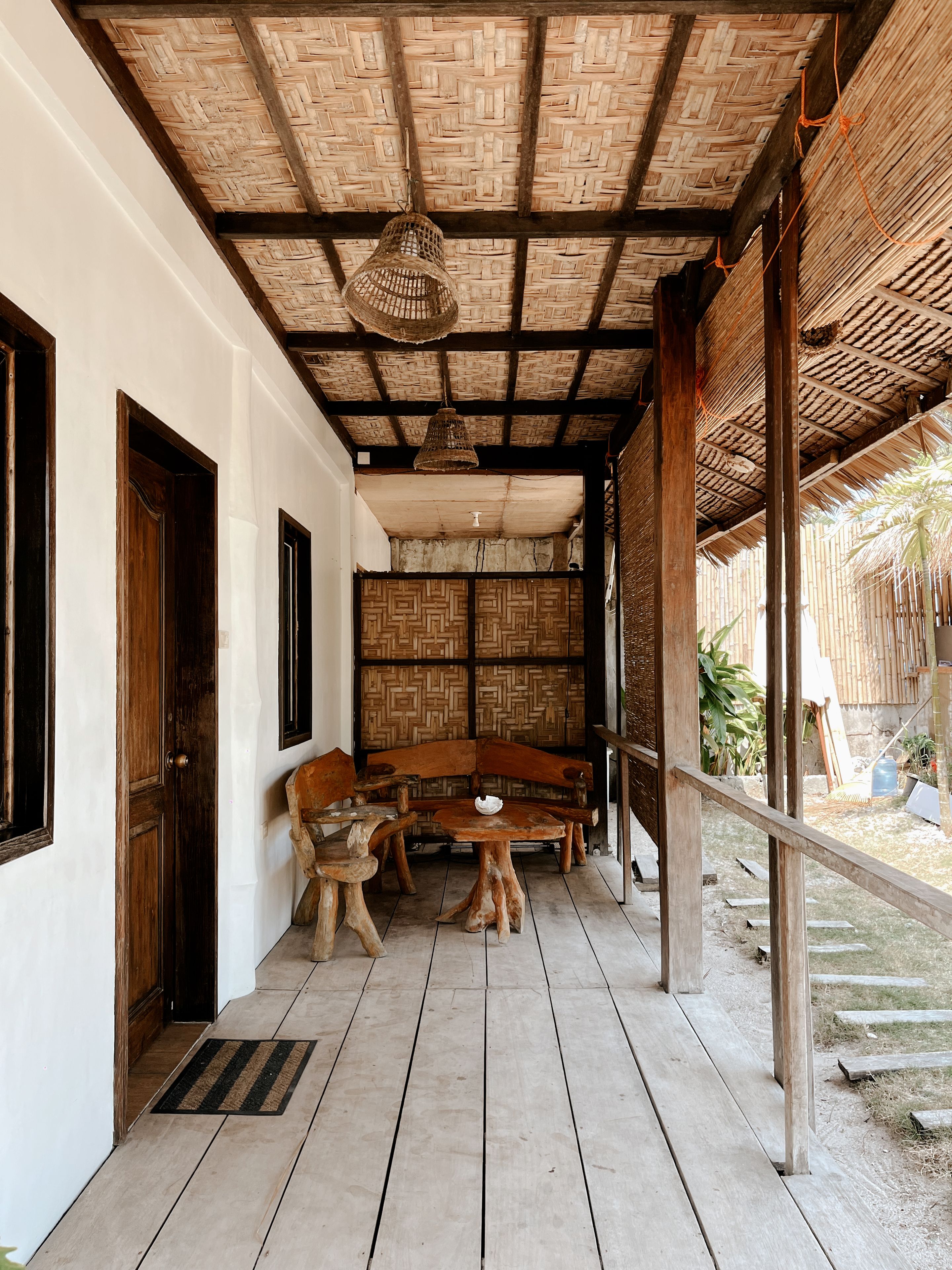 A covered outdoor area with a woven ceiling, wooden furniture, and a thatched wall.