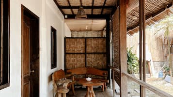Un espacio al aire libre techado con techo tejido, mobiliario de madera y pared de paja.