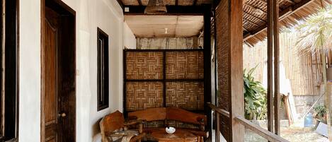 A covered outdoor area with a woven ceiling, wooden furniture, and a thatched wall.