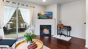 Ein modernes Wohnzimmer mit Kamin, einem Essbereich mit Holztisch und Blick auf einen Balkon mit Gartenmöbeln.