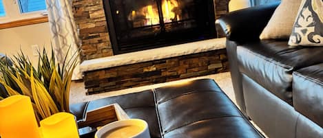 A cozy living room with a fireplace, a leather sofa, and a tray with candles and a mug.