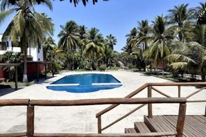 Zona de piscina con terraza de madera y palmeras.