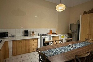 Una cocina compacta con microondas, estufa y refrigerador. Hay una mesa de comedor con sillas y una lámpara colgante.