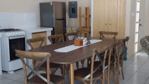 Un comedor con mesa y sillas de madera, una cocina con estufa y refrigerador, y una puerta de madera.