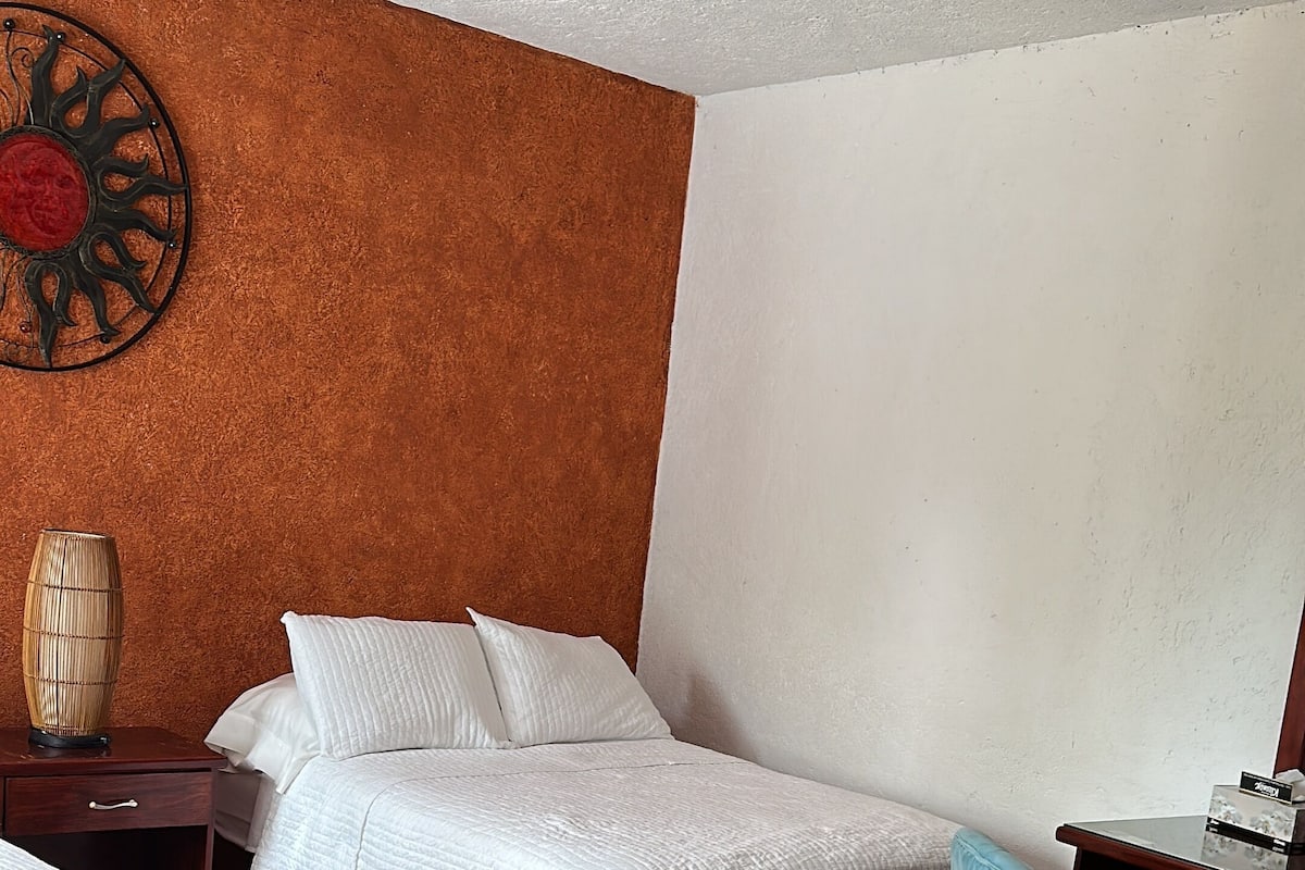 A bedroom with two beds, a nightstand, a lamp, a chair, and a ceiling light fixture.