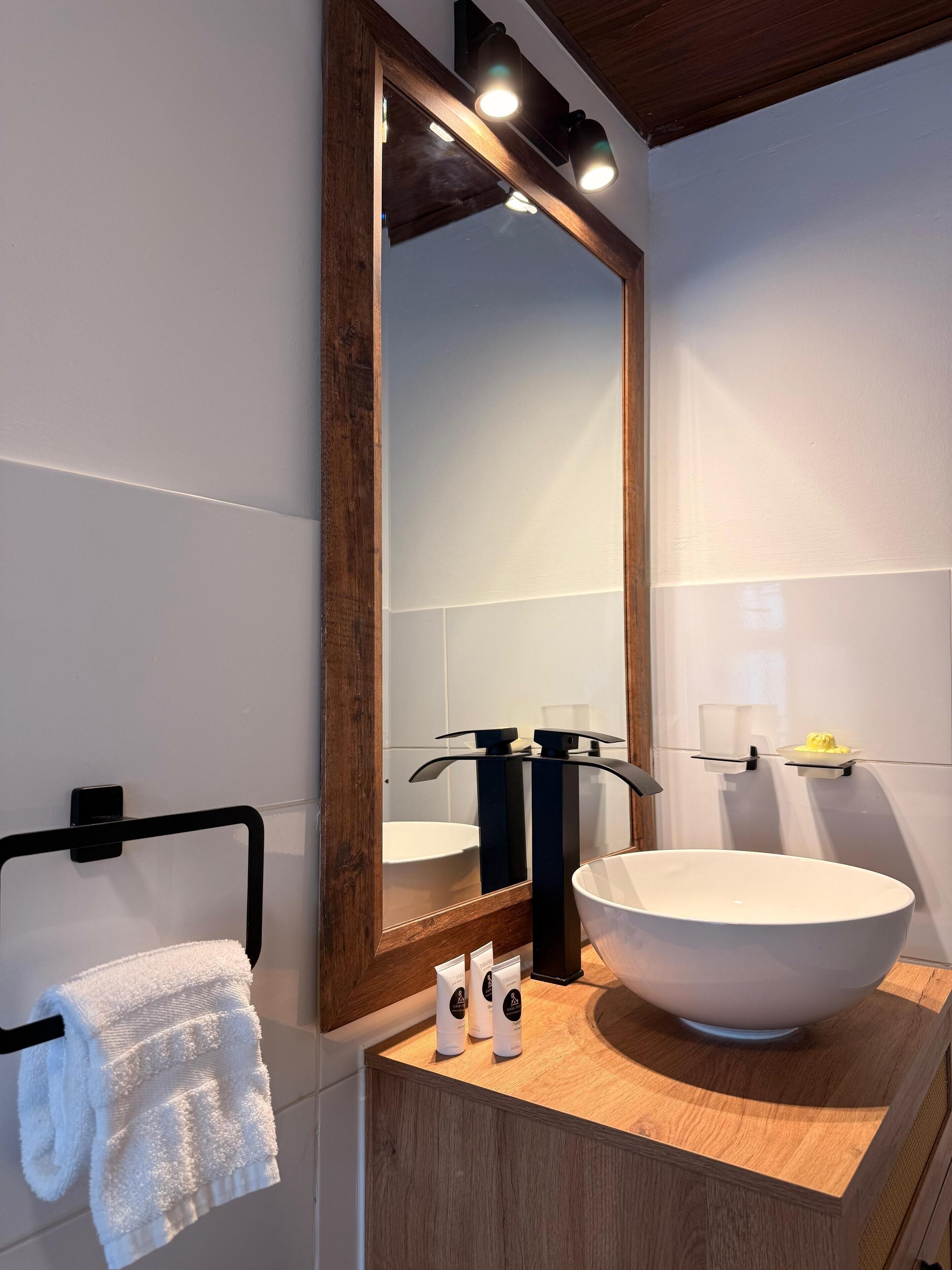 A modern bathroom with a large mirror, a white sink, and a wooden vanity.