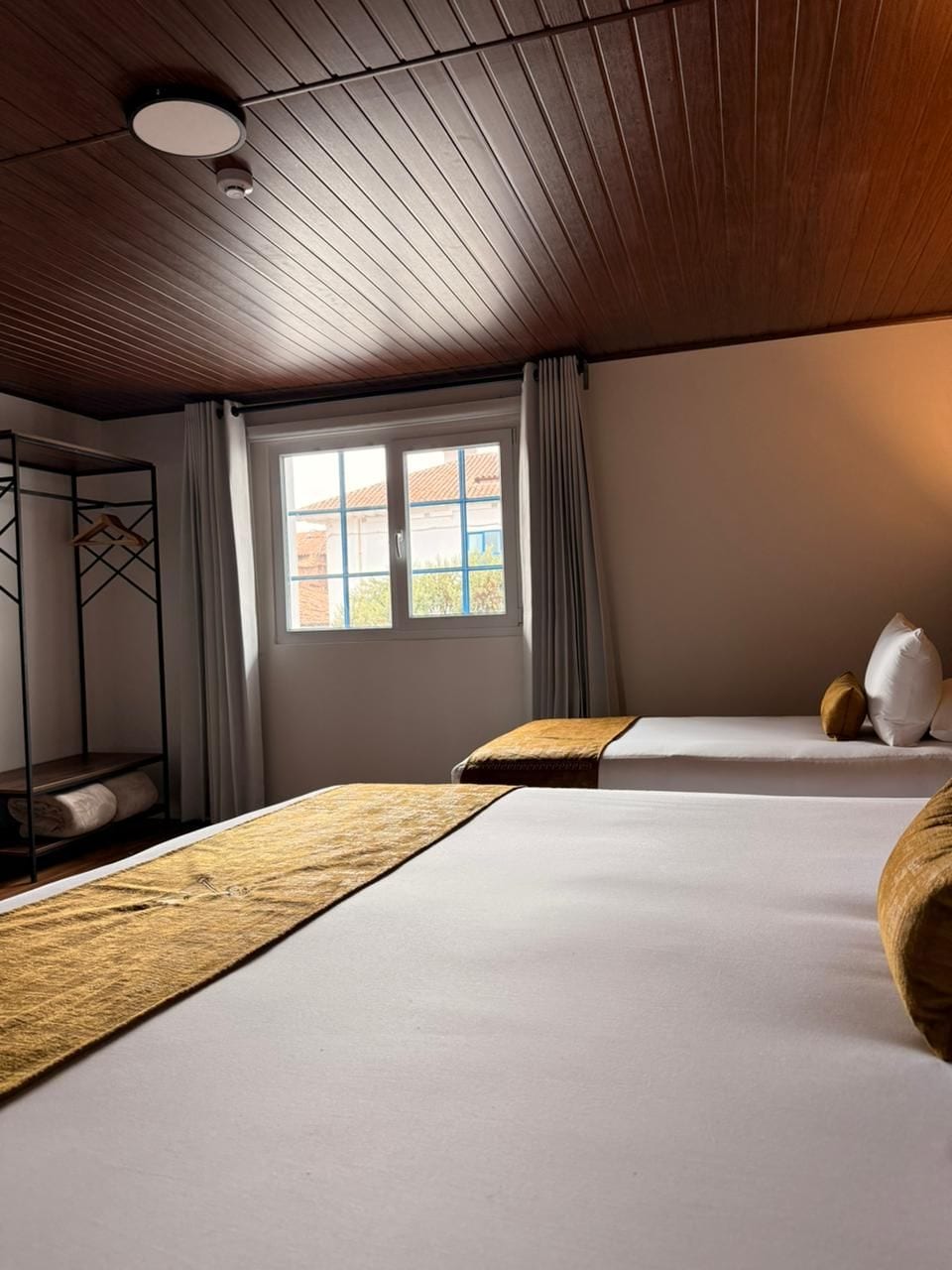 A hotel room with a bunk bed, a window with curtains, and a ceiling with wooden panels.
