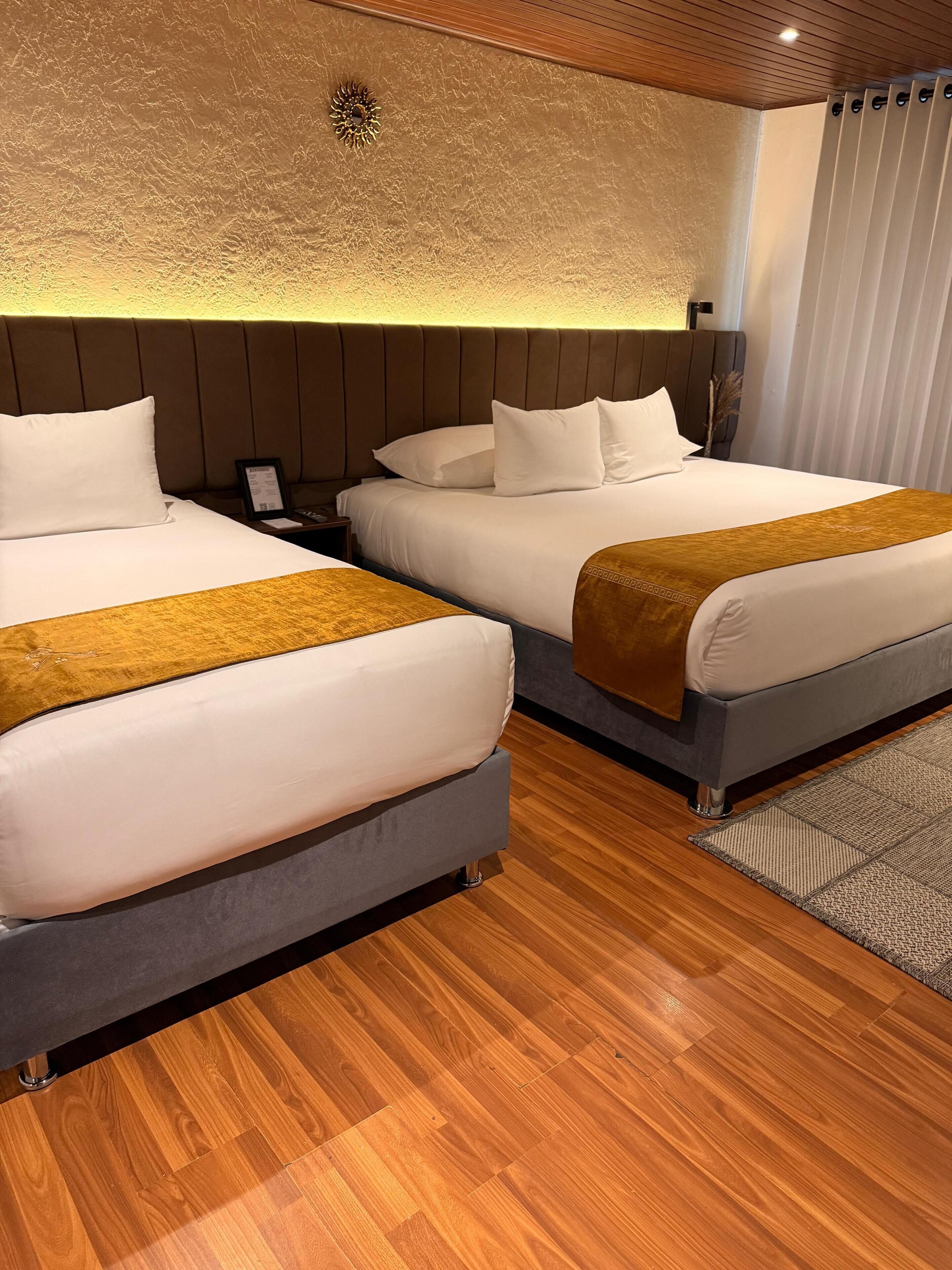 Une chambre d’hôtel avec deux lits, un plancher en bois, une tête de lit moderne et un luminaire fixé au mur.