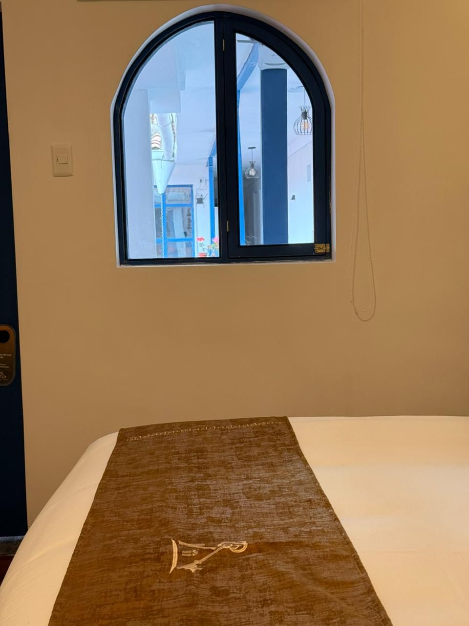 A hotel room with a bed, a window with a view of the outside, and a wall-mounted telephone.