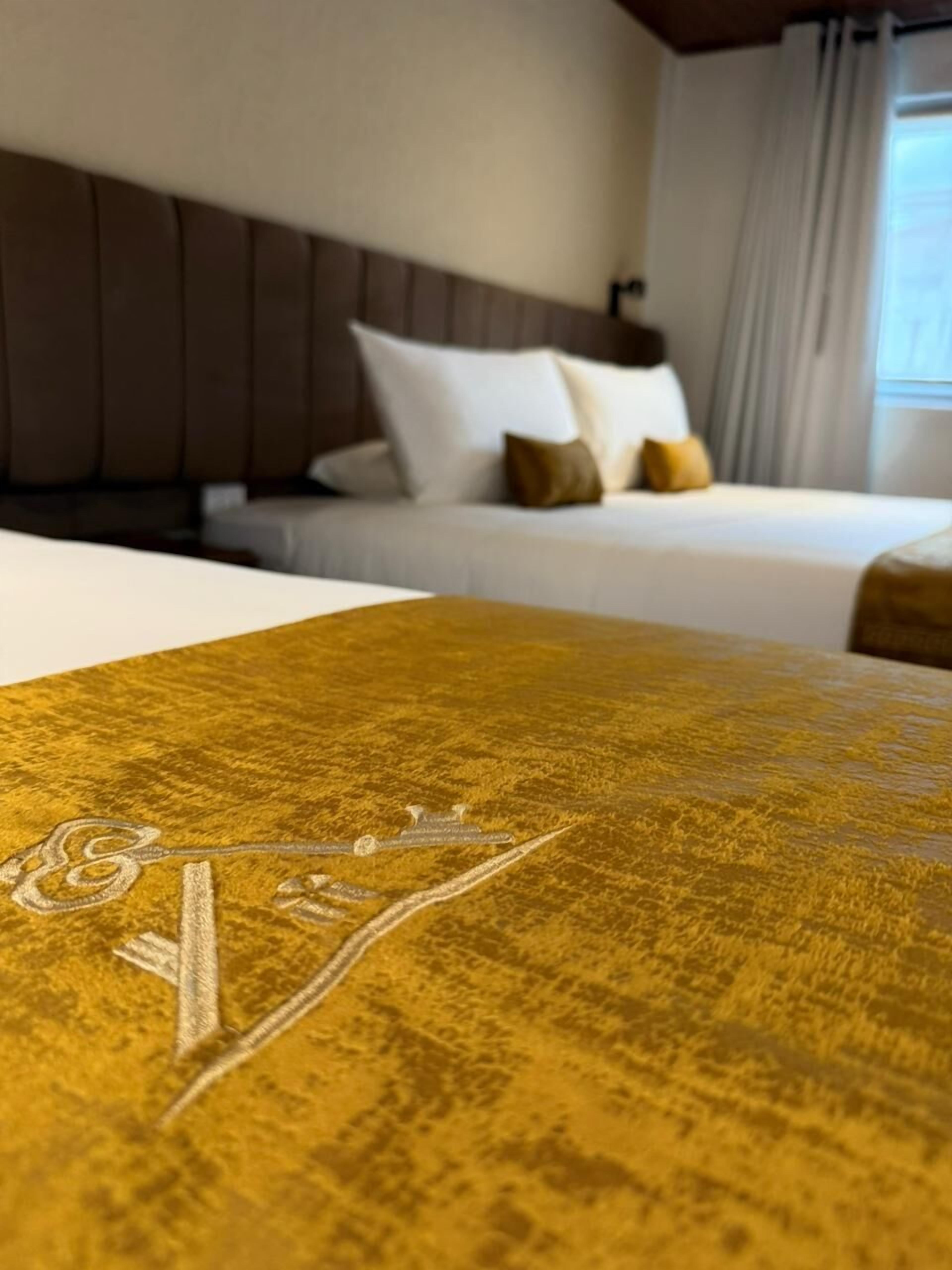 Una habitación de hotel con cama, cabecera y ventana con cortinas.