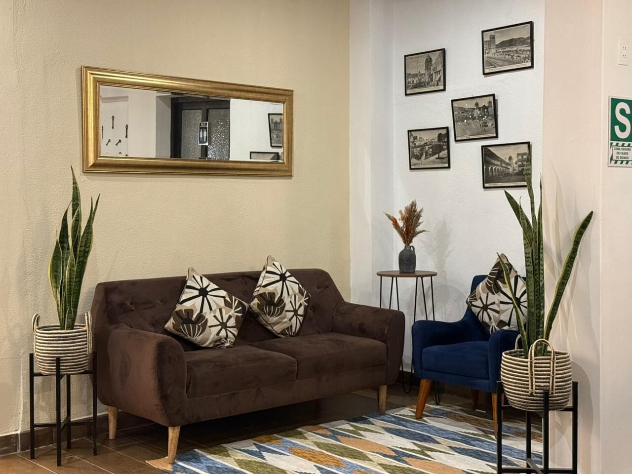 Un salon avec un canapé marron, deux tables d’appoint, un fauteuil bleu et un tapis à motifs.