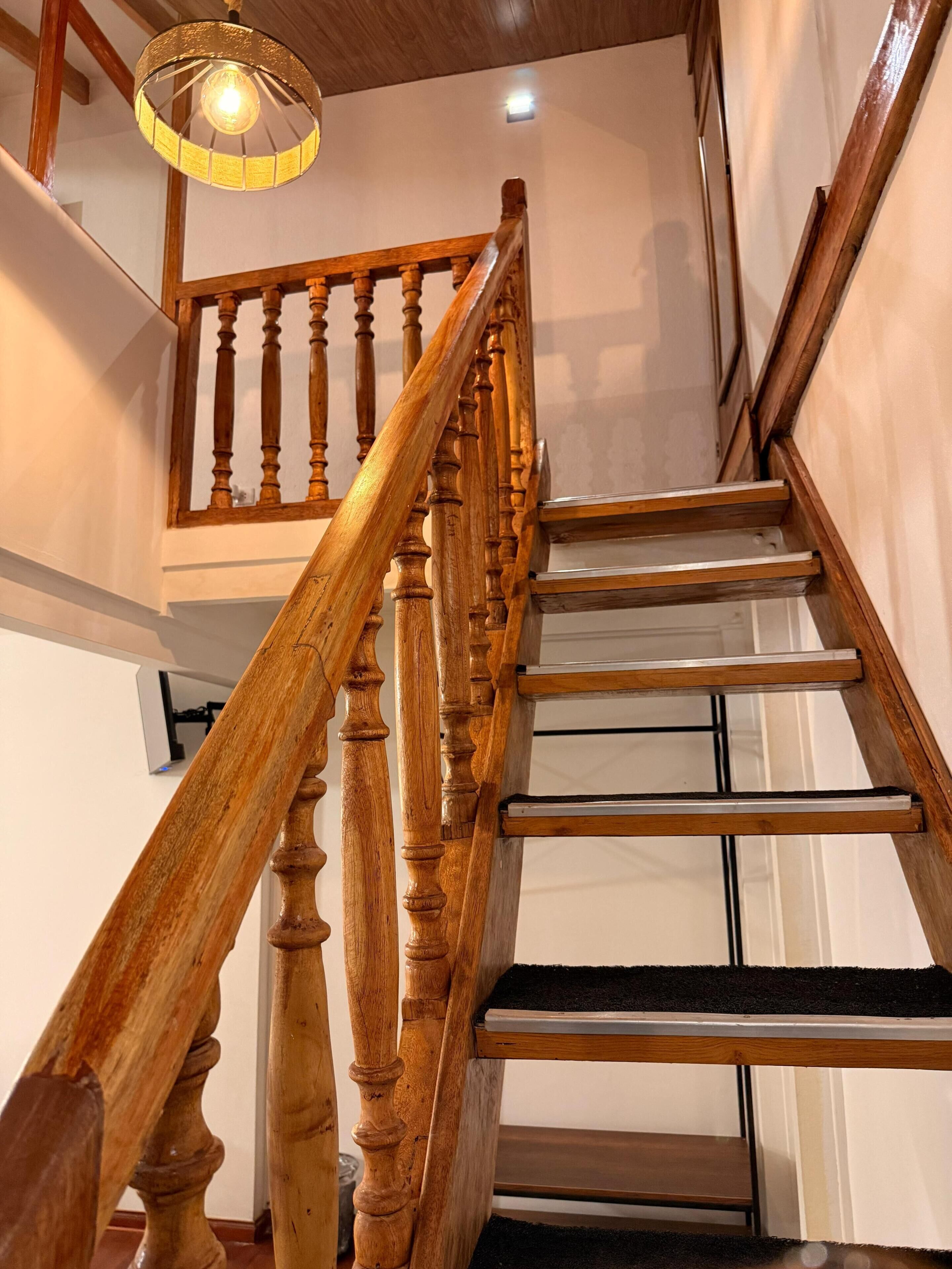 A wooden staircase with a handrail, a light fixture above, and a door at the bottom.