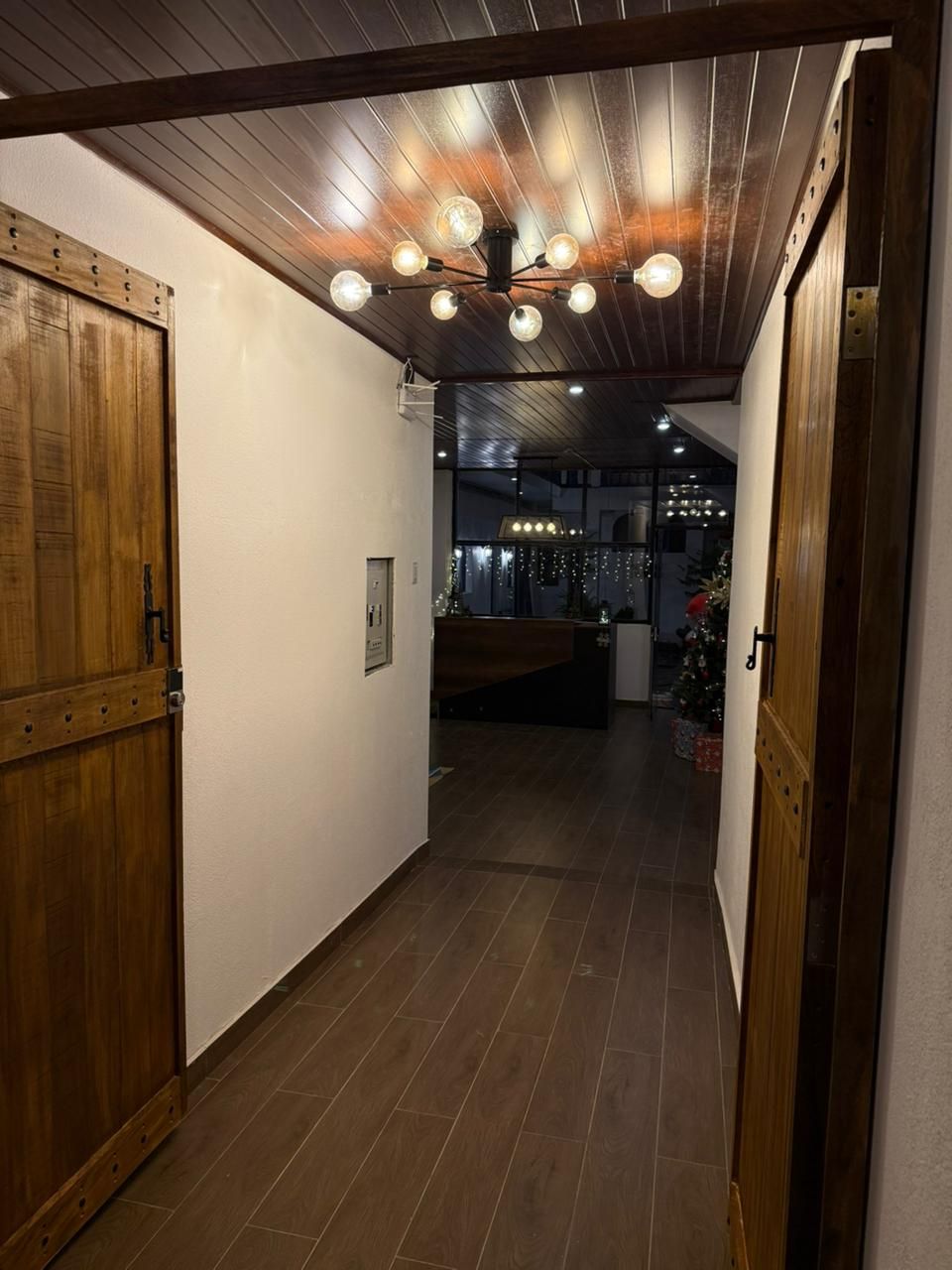Un pasillo con puertas de madera, techo con vigas a la vista y suelo de baldosas.