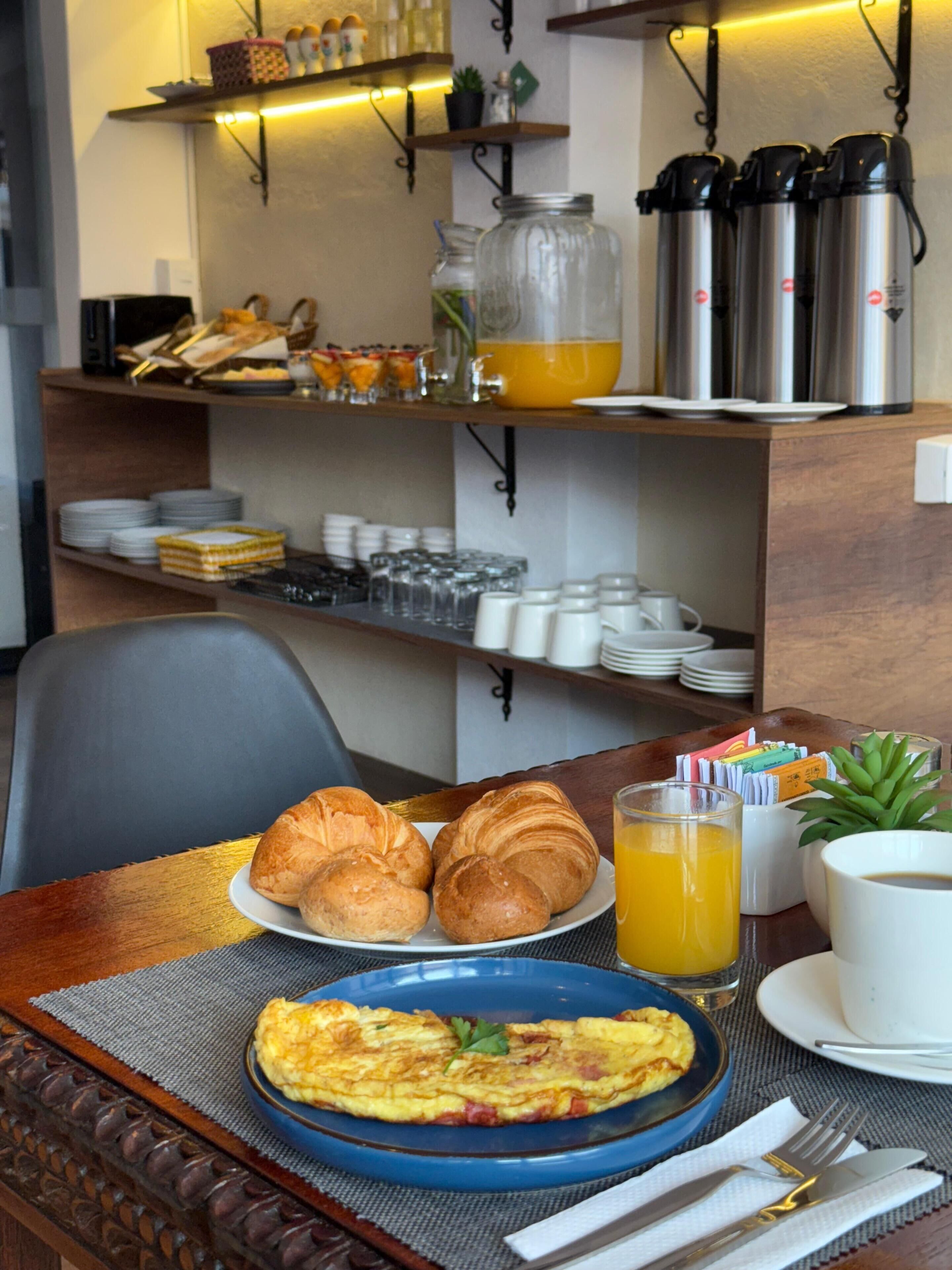 A breakfast setting with croissants, an omelette, orange juice, and coffee cups on a table.