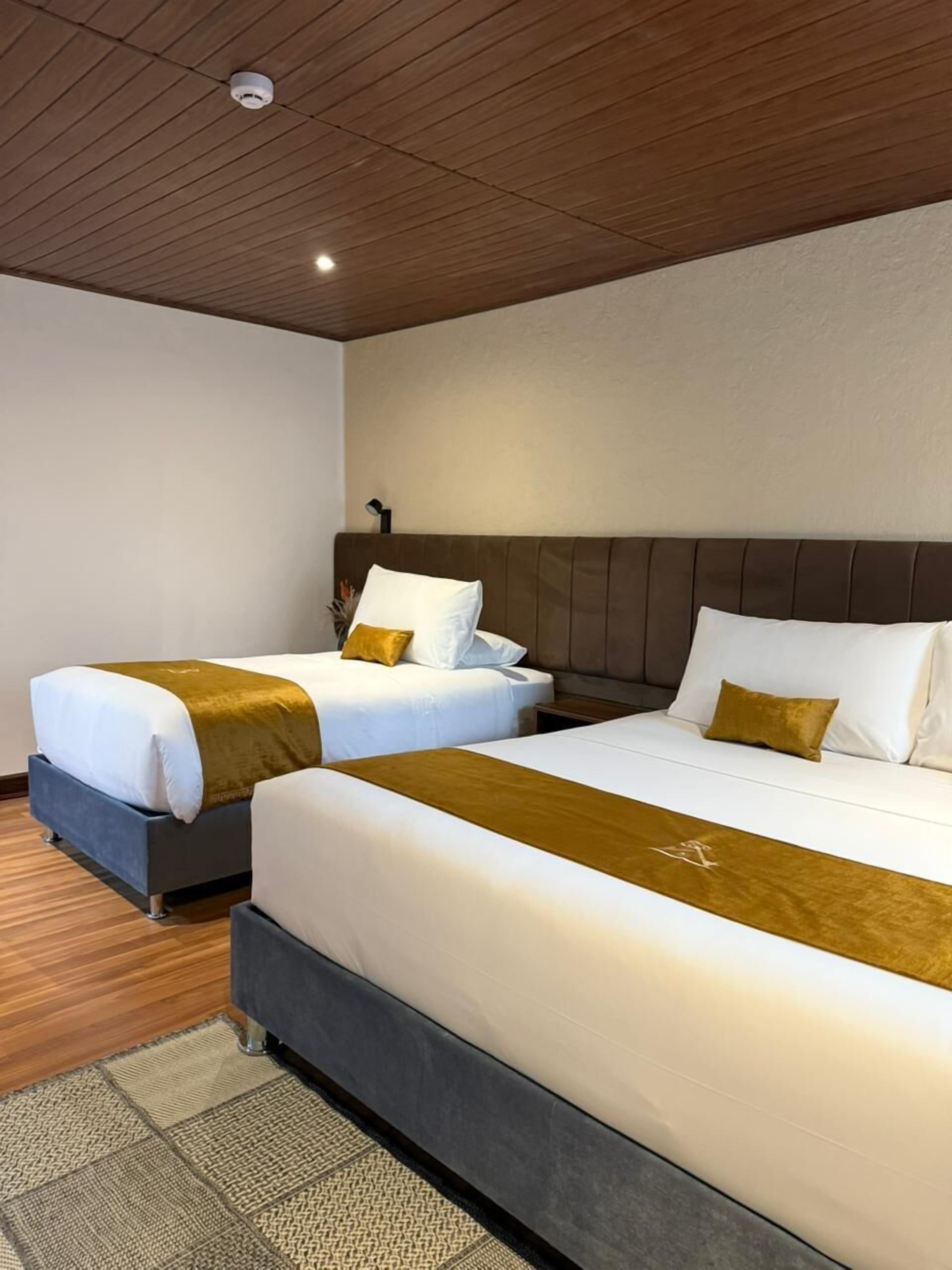 Een hotelkamer met twee bedden, elk voorzien van witte lakens en een bruine plaid. De kamer heeft een houten plafond en een eenvoudig, strak design.