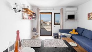 A modern living room with a blue sofa, a small table, and a balcony with a view. - Capistrano Village, 1 Bedroom (Nerja)