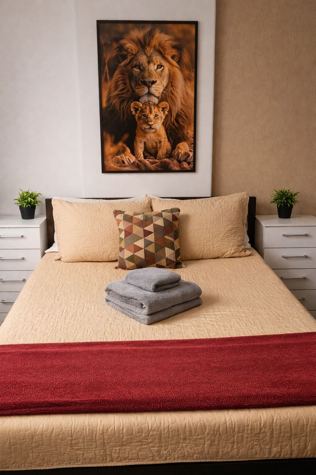 Ein Schlafzimmer mit einem Bett, Kissen, einer Decke und einem Bilderrahmen mit Löwen an der Wand.