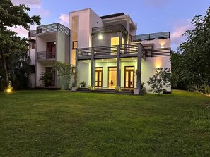 Ein modernes, zweistöckiges Haus mit flachem Dach, großen Fenstern und einem gepflegten Rasen.