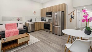 A modern kitchen with stainless steel appliances, a dining area with a white table and chairs, and a living area with a black sofa and a pink throw blanket. - Arcade, Great Coffee, 80 min Banff, Brand New (Calgary)