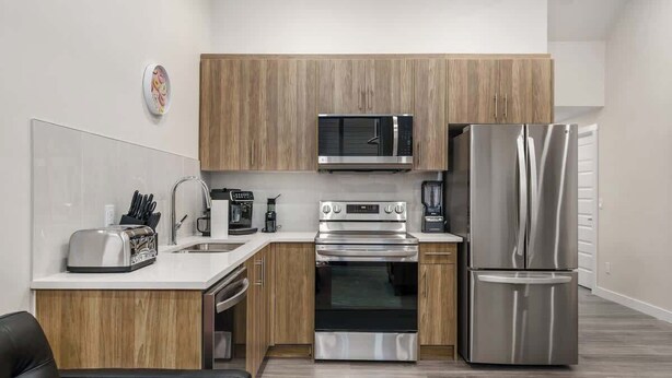 A modern kitchen with wooden cabinets, stainless steel appliances, a toaster, and a coffee maker. - Arcade, Great Coffee, 80 min Banff, Brand New (Calgary)