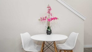 A round table with two white chairs, a potted plant with pink flowers, and a wooden floor. - Arcade, Great Coffee, 80 min Banff, Brand New (Calgary)