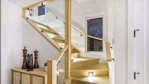 A wooden staircase with glass railings, a small cabinet with decorative items, and a window with a view of trees. - Trendy Bridgeland | Fireplace | King Beds | AC (Calgary)