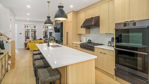 A modern kitchen with a central island, stainless steel appliances, and pendant lighting. - Trendy Bridgeland | Fireplace | King Beds | AC (Calgary)