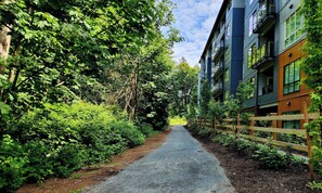 A pathway flanked by dense greenery and a multi-story building with balconies. - Enchanted Rooftop Escape | Beautiful Sunsets (Surrey)