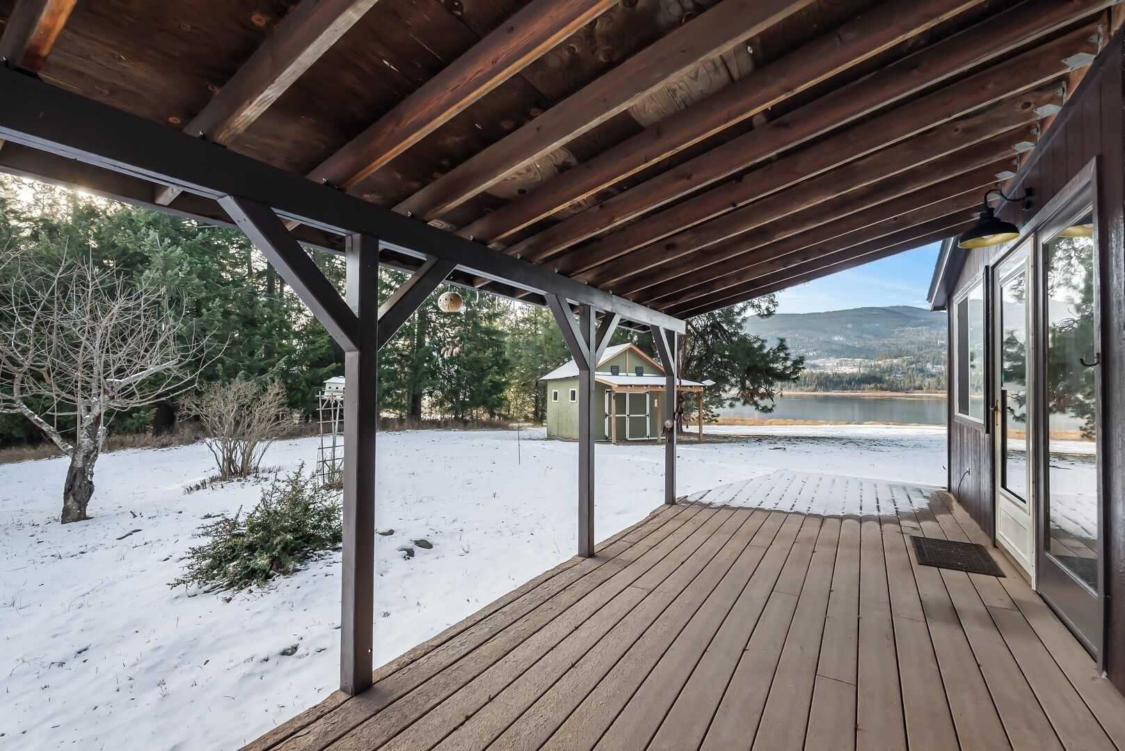 Une terrasse en bois couverte, d’où l’on peut admirer un lac, et une petite cabane en arrière-plan.