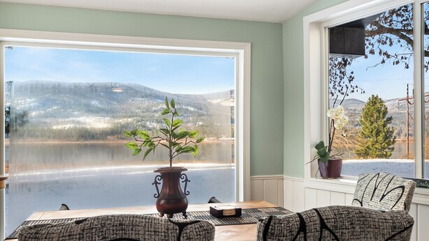 Un coin repas avec vue sur un lac et des montagnes, un vase avec une plante et deux chaises à motifs.