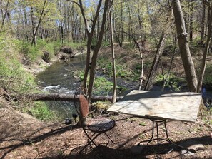 Un campament amb una cadira de metall i una taula al costat d'un riu en un bosc.