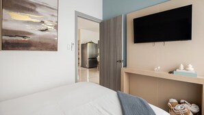 Et moderne hotelværelse med en seng, et fladskærms-tv på væggen, et billede på væggen og et træskab nedenunder.