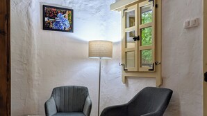 Een kamer met twee grijze fauteuils, een klein rond tafeltje, een vloerlamp en een raam met uitzicht op groen.