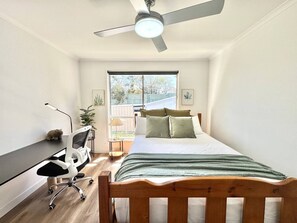 Een slaapkamer met een bed, bureau, stoel en een plafondventilator.