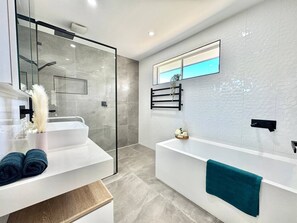 Een moderne badkamer met een douchecabine van glas, een witte badkuip en een grote spiegel.