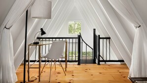 Een tent met houten vloer, een witte stoel, een bureau met lamp en een raam met uitzicht op groen.