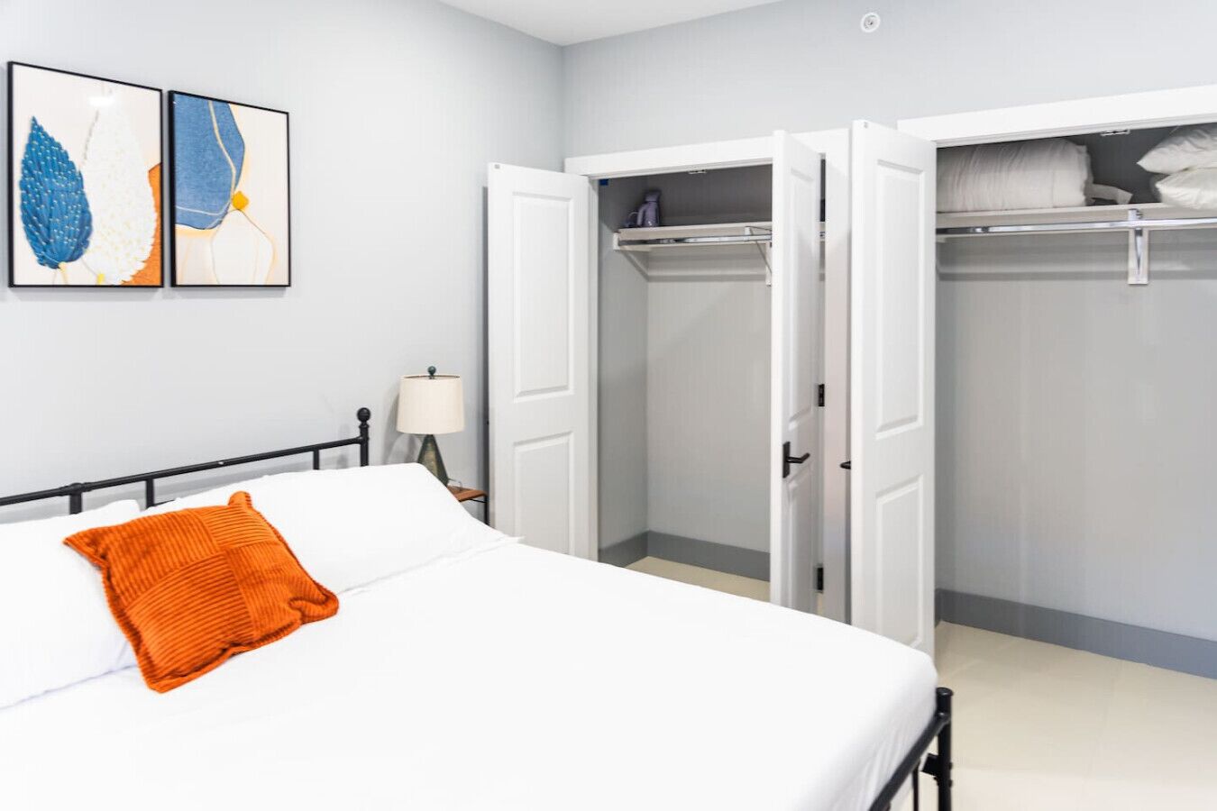Un dormitorio con cama, armario abierto y mesita de noche con lámpara.