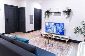 Moderni olohuone, jossa on litteänäyttöinen televisio, tummat ovet, valkoinen konsolipöytä ja kuviollinen matto.