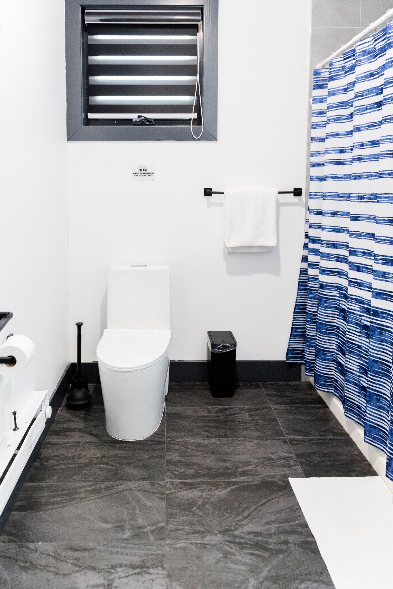 Un baño con inodoro, un cubo de basura, toallero y cortina de ducha.