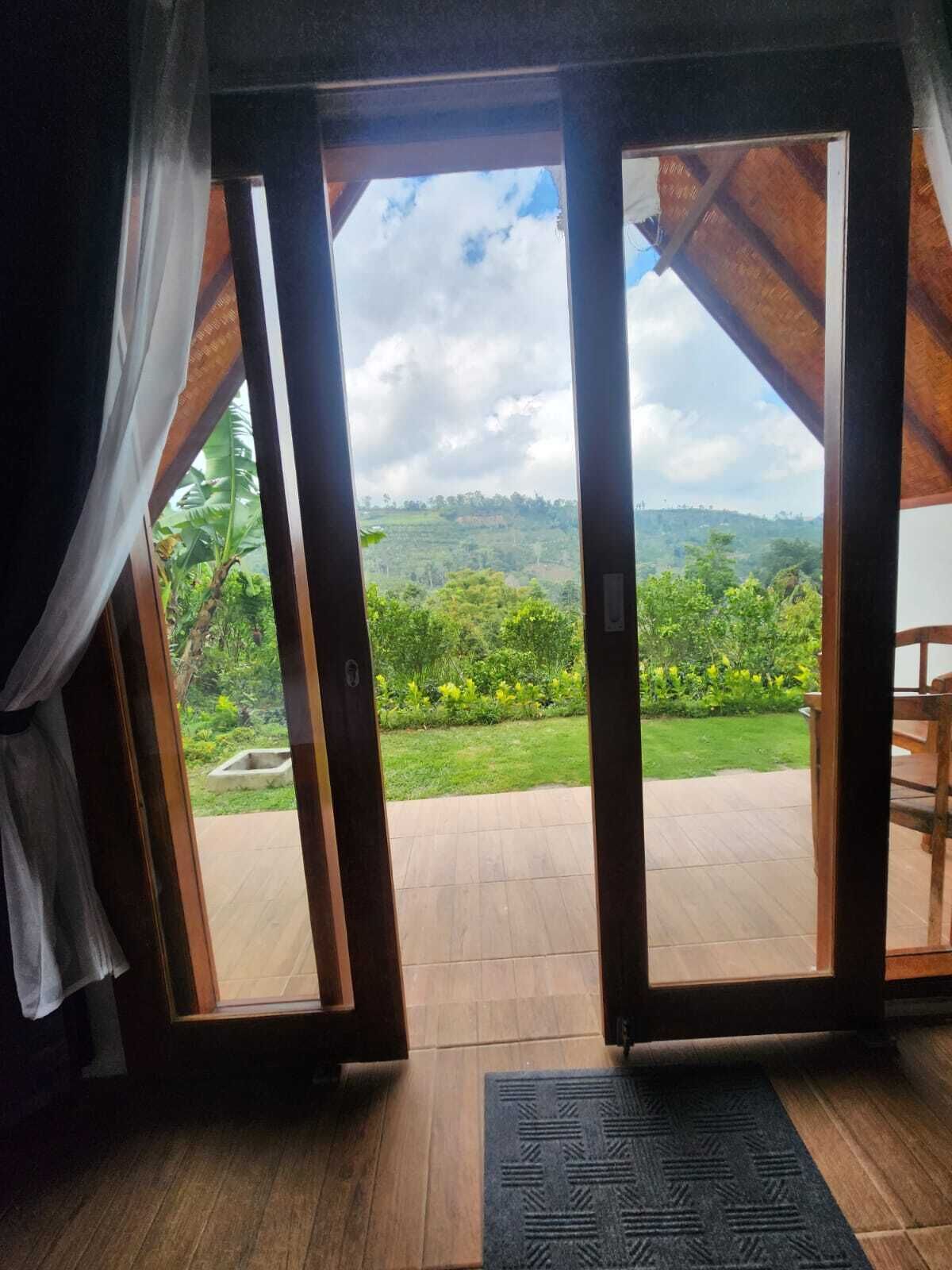 Una habitación con piso de madera, un felpudo negro y vista a un paisaje verde exuberante a través de puertas correderas abiertas.