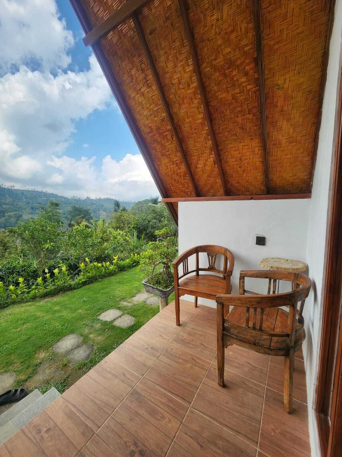 A room with a view of a lush garden and hills. There are two wooden chairs and a small round table.