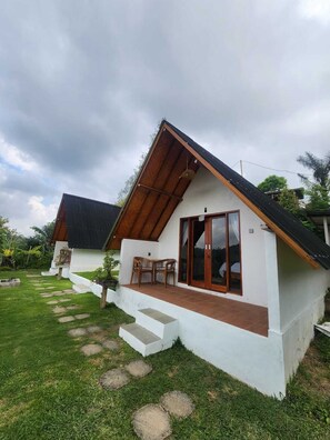 A single-story house with a sloped roof, a front porch with a table and chairs, and a paved pathway leading to the entrance. - Pondok Kanginan (Pelaga)