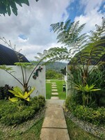 Un sendero conduce a una casa con vistas a un exuberante jardín y colinas distantes.