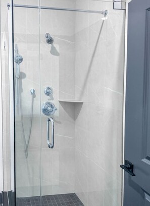 Eine Duschkabine mit Glaswänden, einem Chrom-Duschkopf, einer Handbrause und einer Handbrause mit flexiblen Schlauch.